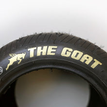 Image illustrates the the goat tire in gold for the onewheel, that's sold exclusively from flight fins, featuring a closeup of the black tirewith the text the goat and vector image of a oat in the color gold set in front of a white background.