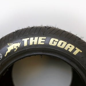 Image illustrates the the goat tire in gold for the onewheel, that's sold exclusively from flight fins, featuring a closeup of the black tirewith the text the goat and vector image of a oat in the color gold set in front of a white background.